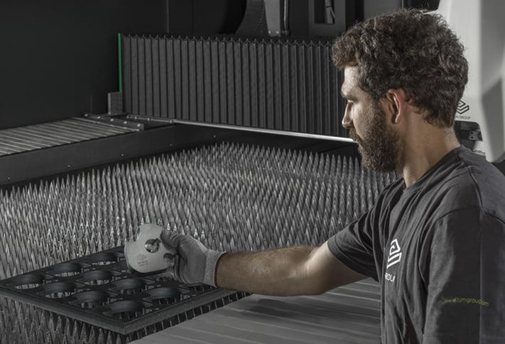 Operador retirando la pieza cortada de una máquina de corte por láser con motores lineales. Fuelles de aluminio protegiendo las guías de los motores lineales frente a él